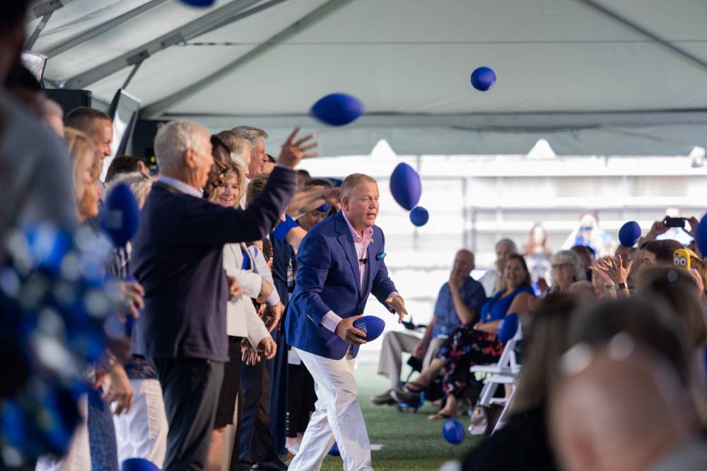 Guests on stage throwing footballs into the crowd at the Jamie Hosford Football Center dedication.